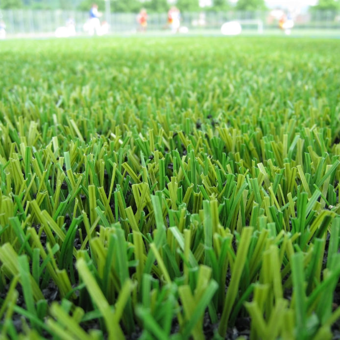 Astro turf playing field with children playing soccer in the distance.